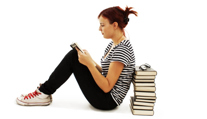 Teenage girl reading and leaning against a stack of books