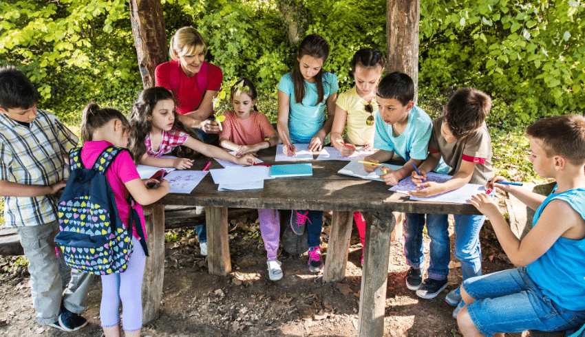 School trips image of children standing around table outside, filling out worksheets