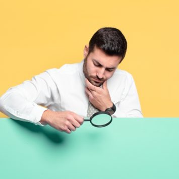 photo of besuited man inspecting a plain surface with a magnifying glass, representing Ofsted outstanding schools downgraded