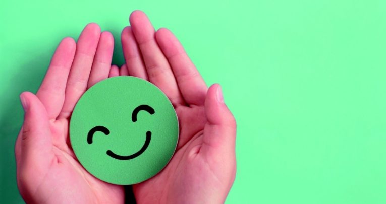 Two hands cradling green smiley emoji, representing wellbeing in schools