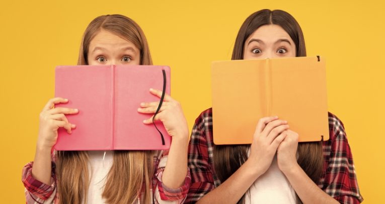 Two girls peeking over books, representing teaching English Literature