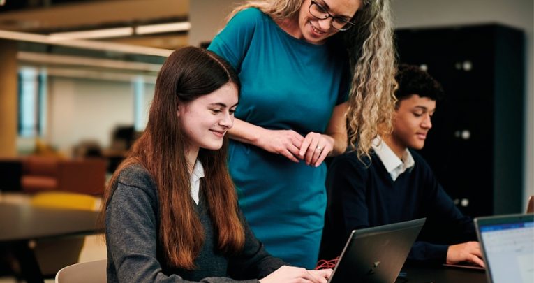 Photo of two students with laptops and a teacher in the classroom, representing Online Education Accreditation Scheme