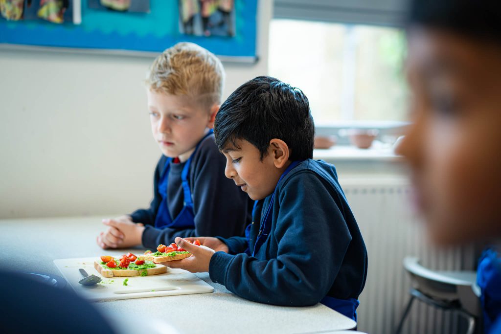 Two primary school boys in Leiths Academy aprons preparing a sandwich in a classroom