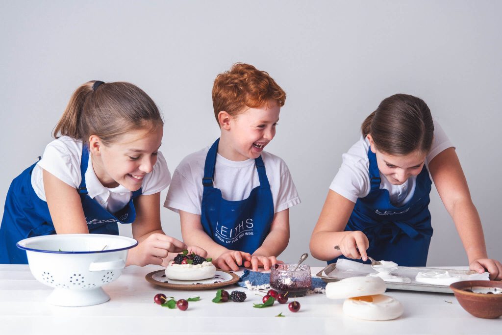 Three primary school children in Leiths Academy aprons preparing a dessert