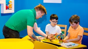 A workshop leader helping two primary school boys build with LEGO bricks