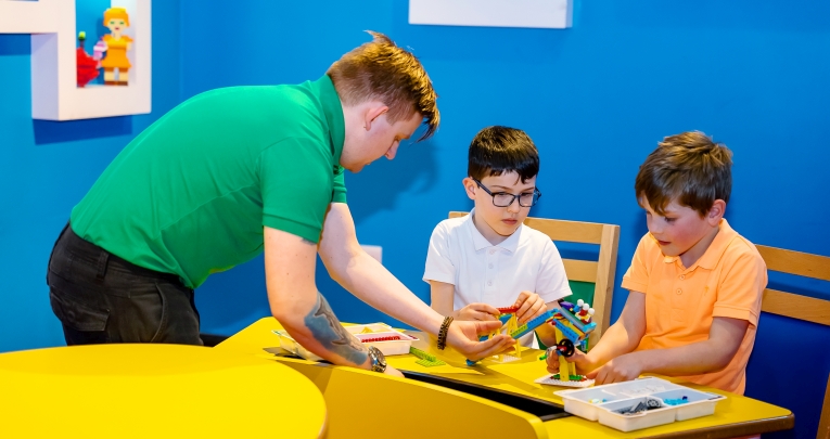 A workshop leader helping two primary school boys build with LEGO bricks