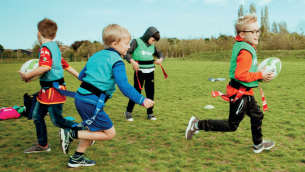 Primary school boys on a school field playing rugby for a PE lesson