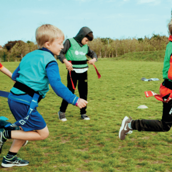 Primary school boys on a school field playing rugby for a PE lesson