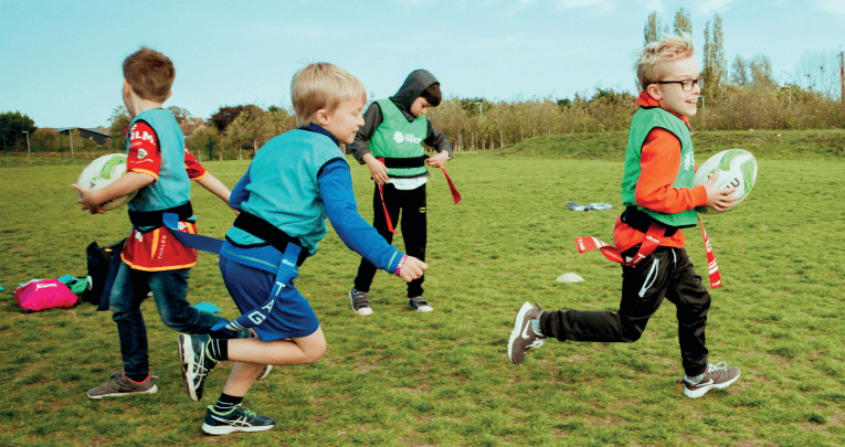 Primary school boys on a school field playing rugby for a PE lesson