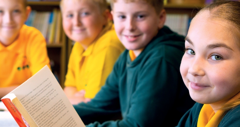 A school girl reading book alongside three school boys