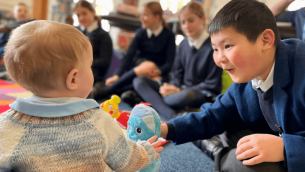 A picture of a school boy passing a toy to a baby