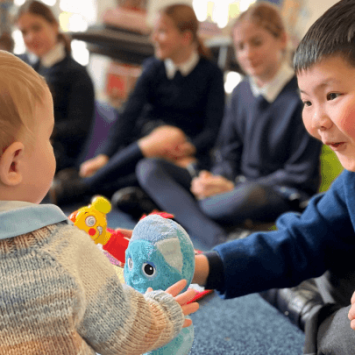 A picture of a school boy passing a toy to a baby