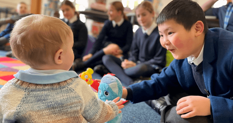 A picture of a school boy passing a toy to a baby