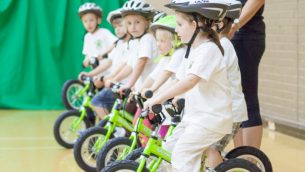 A group of schoolchildren learning to ride bikes indoors