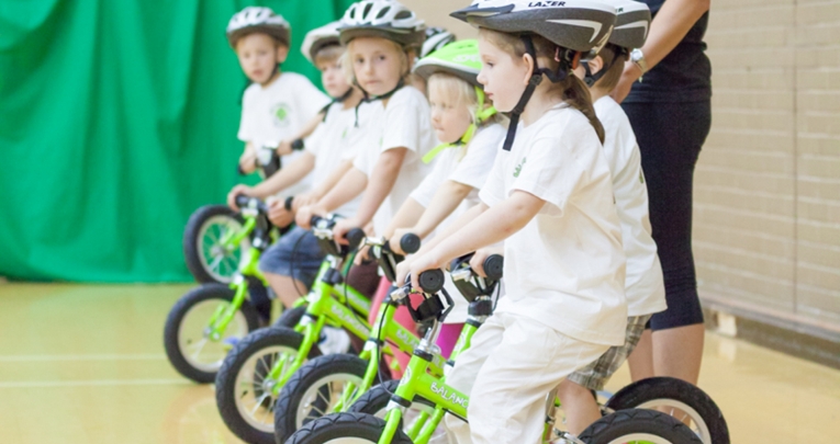 A group of schoolchildren learning to ride bikes indoors