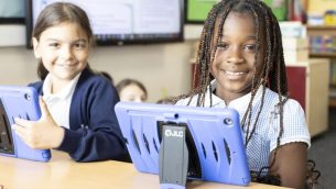 Two school girls with tablets sitting at a desk