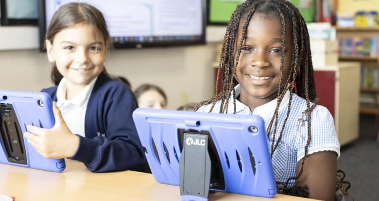 Two school girls with tablets sitting at a desk