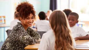 A primary school teacher speaking to a pupil in a classroom