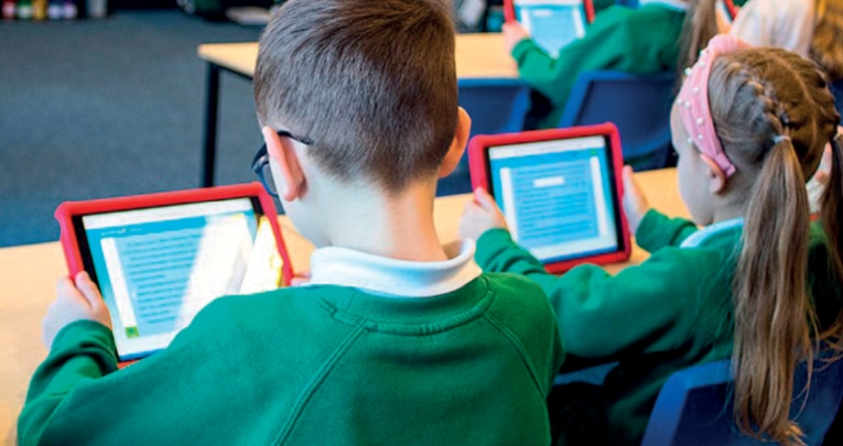 Primary school students sitting and working on tablets