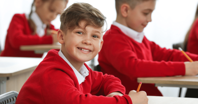 Smiling boy in school uniform doing SATs reading paper