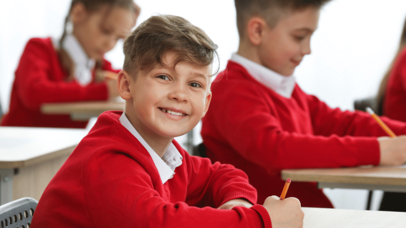 Smiling boy in school uniform doing SATs reading paper