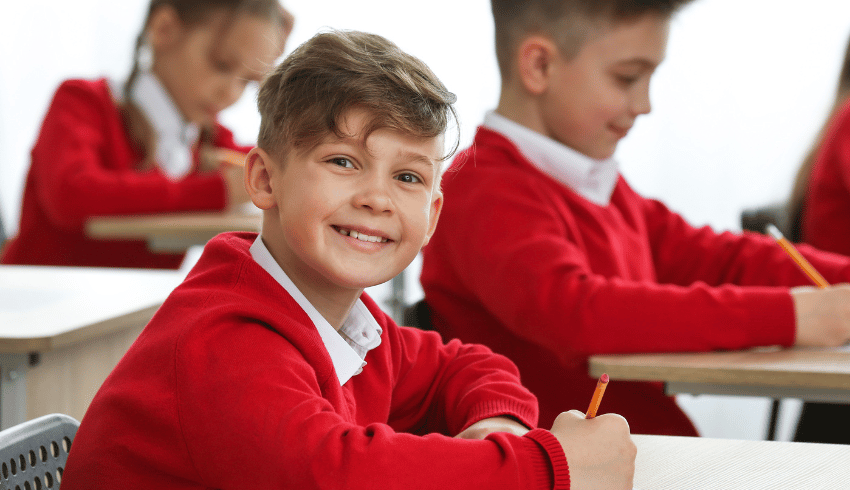 Smiling boy in school uniform doing SATs reading paper