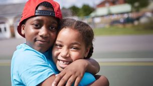 Two smiling primary school pupils hugging each other