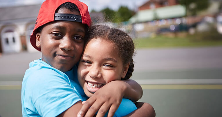 Two smiling primary school pupils hugging each other