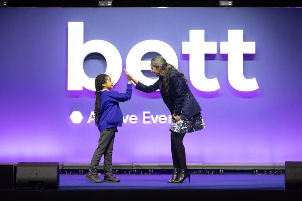 Schoolchild and adult high-fiving in front of large Bett Show sign