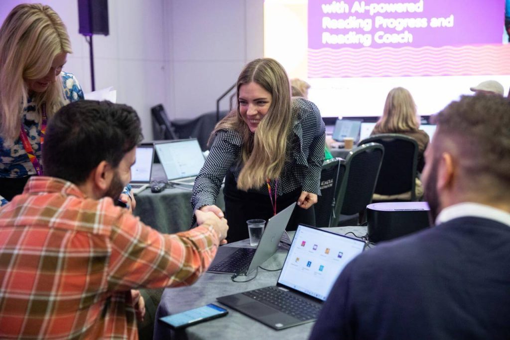 Two professionals shaking hands over laptops at Bett Show