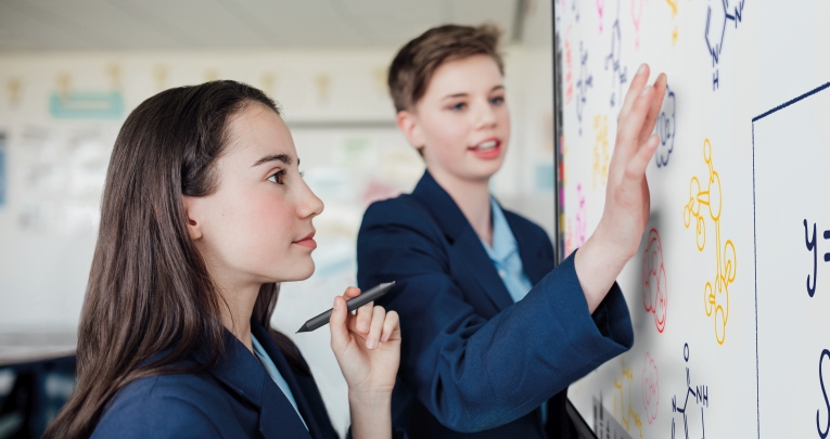 Two secondary school students standing next to an interactive whiteboard