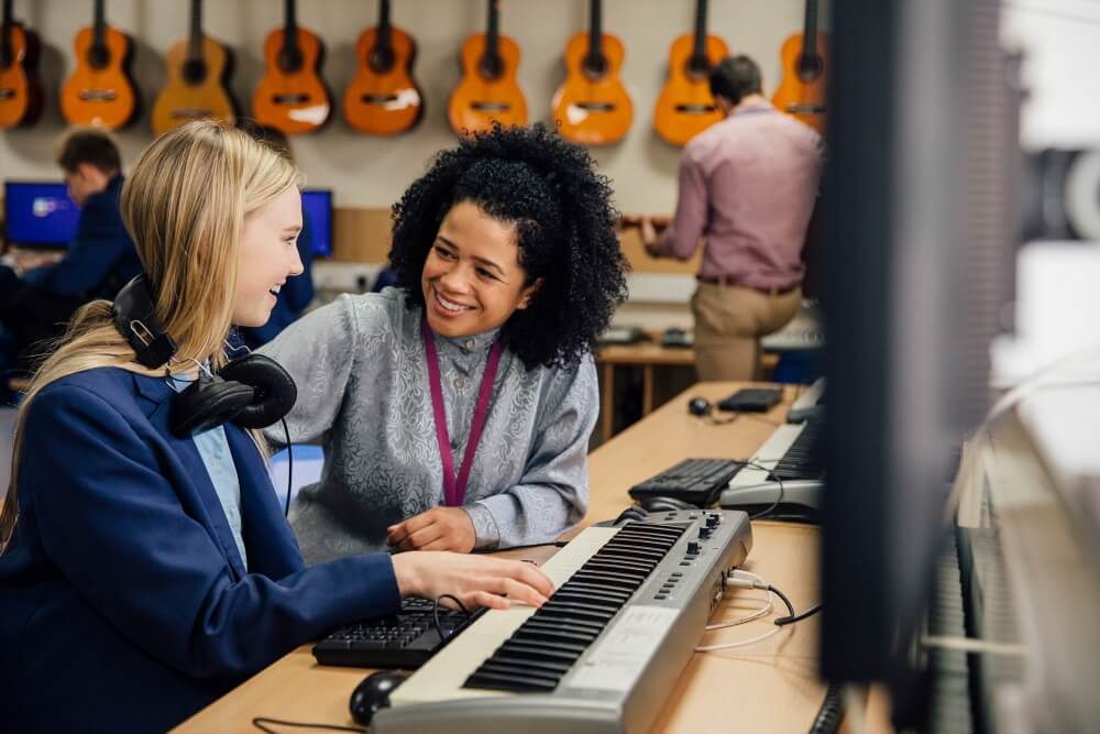 A school teacher sitting with a student in a music classroom