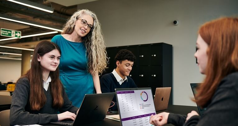 Two secondary school girls working on laptops with a teacher